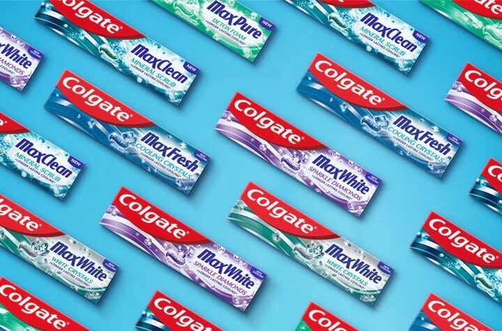 Dažādu Colgate zobu pastu iepakojumi, tostarp Max White, Max Fresh un Max Clean, izkārtoti diagonālā rakstā uz zila fona.